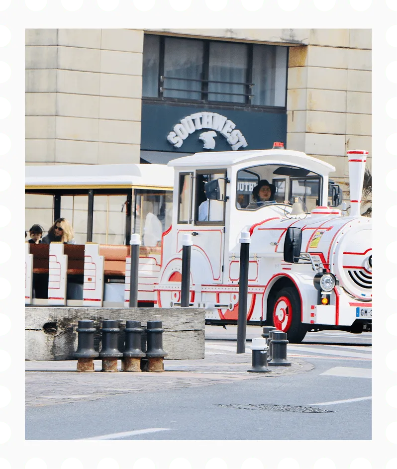 White and red tourist tram with passengers driving on a city street in front of a building with a 'SOUTHWEST' sign.