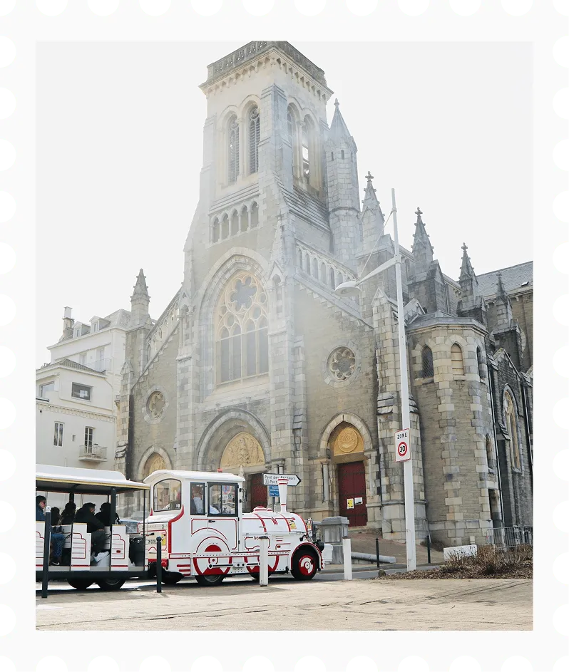Small tourist train with passengers parked in front of a historic stone church with stained glass windows and a tall tower.